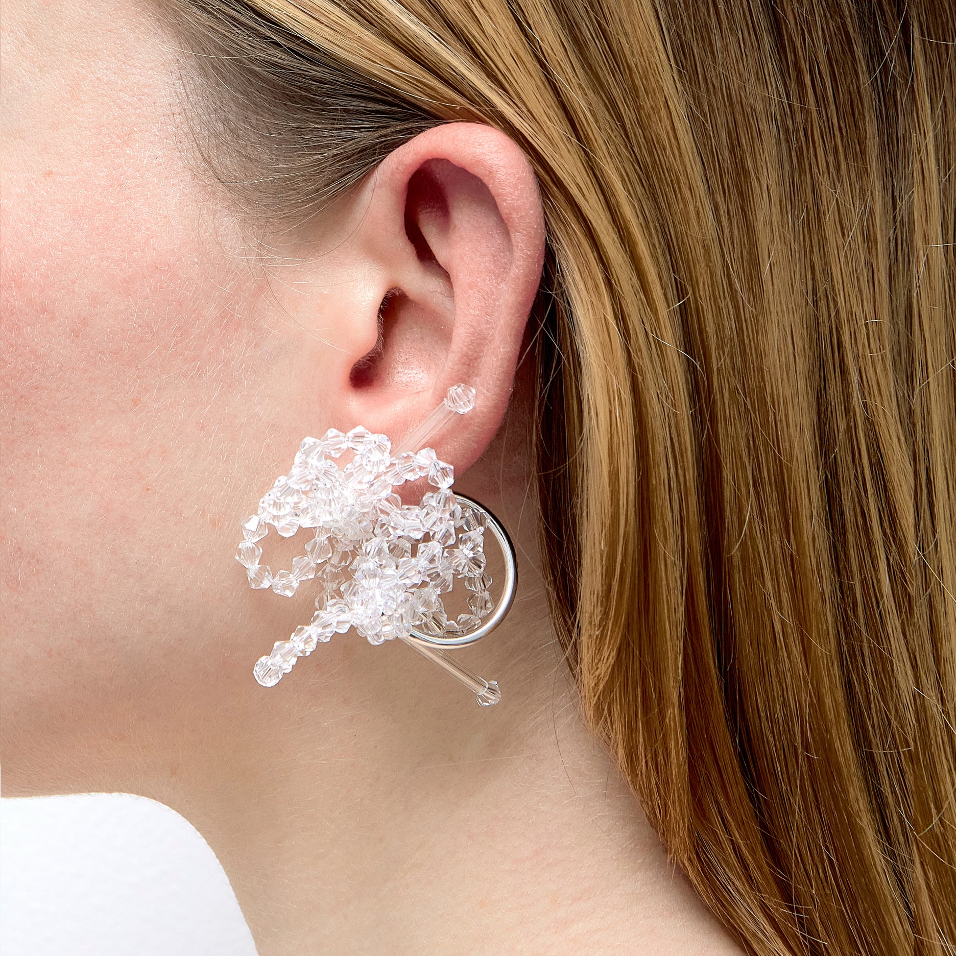 Close-up of a person wearing a silver earring with clear beads.