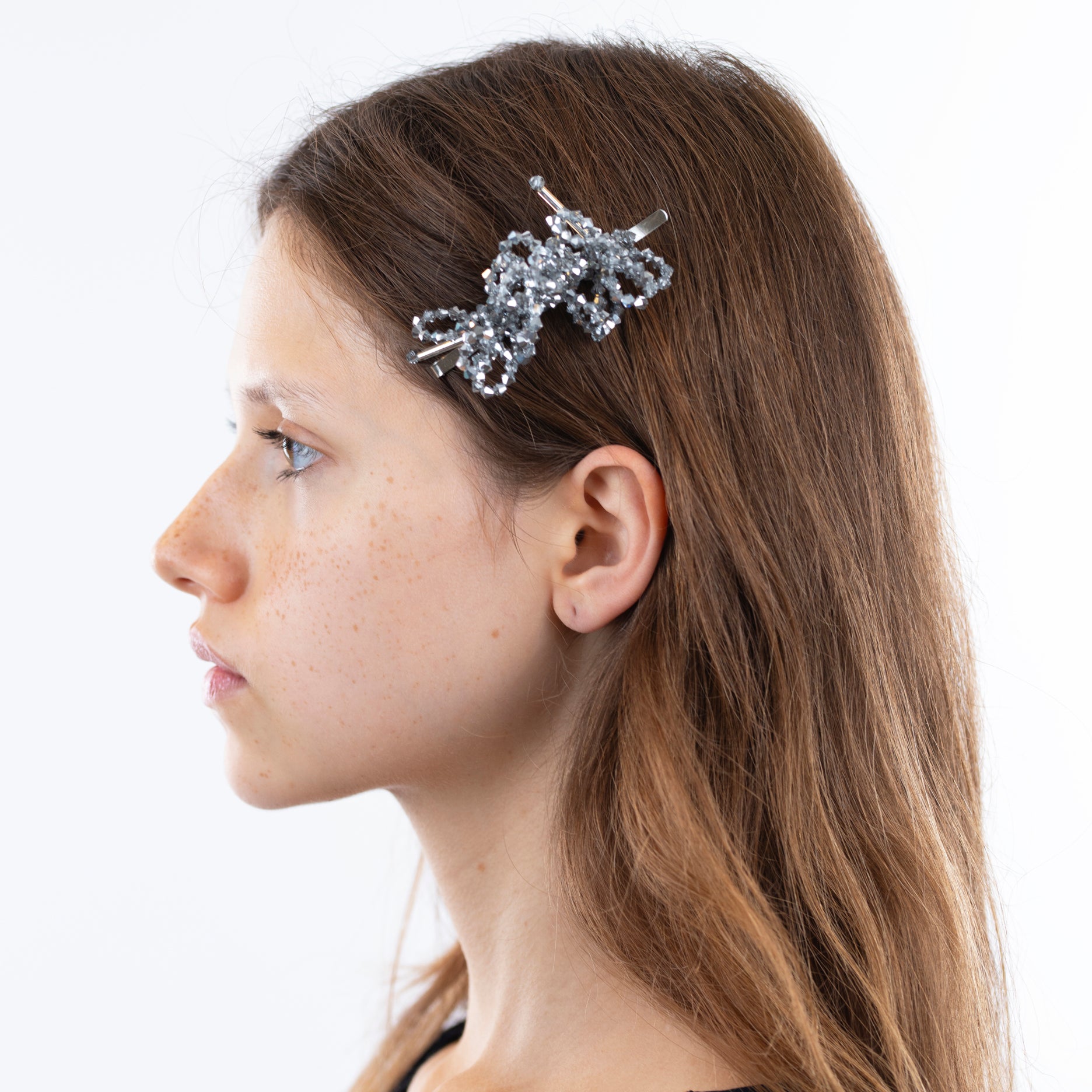 A silver, floral-inspired pearl hairclip worn by a woman with brown hair, viewed from the side
