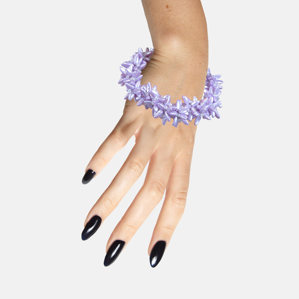 Hand wearing a purple floral statement beaded bracelet on a white background