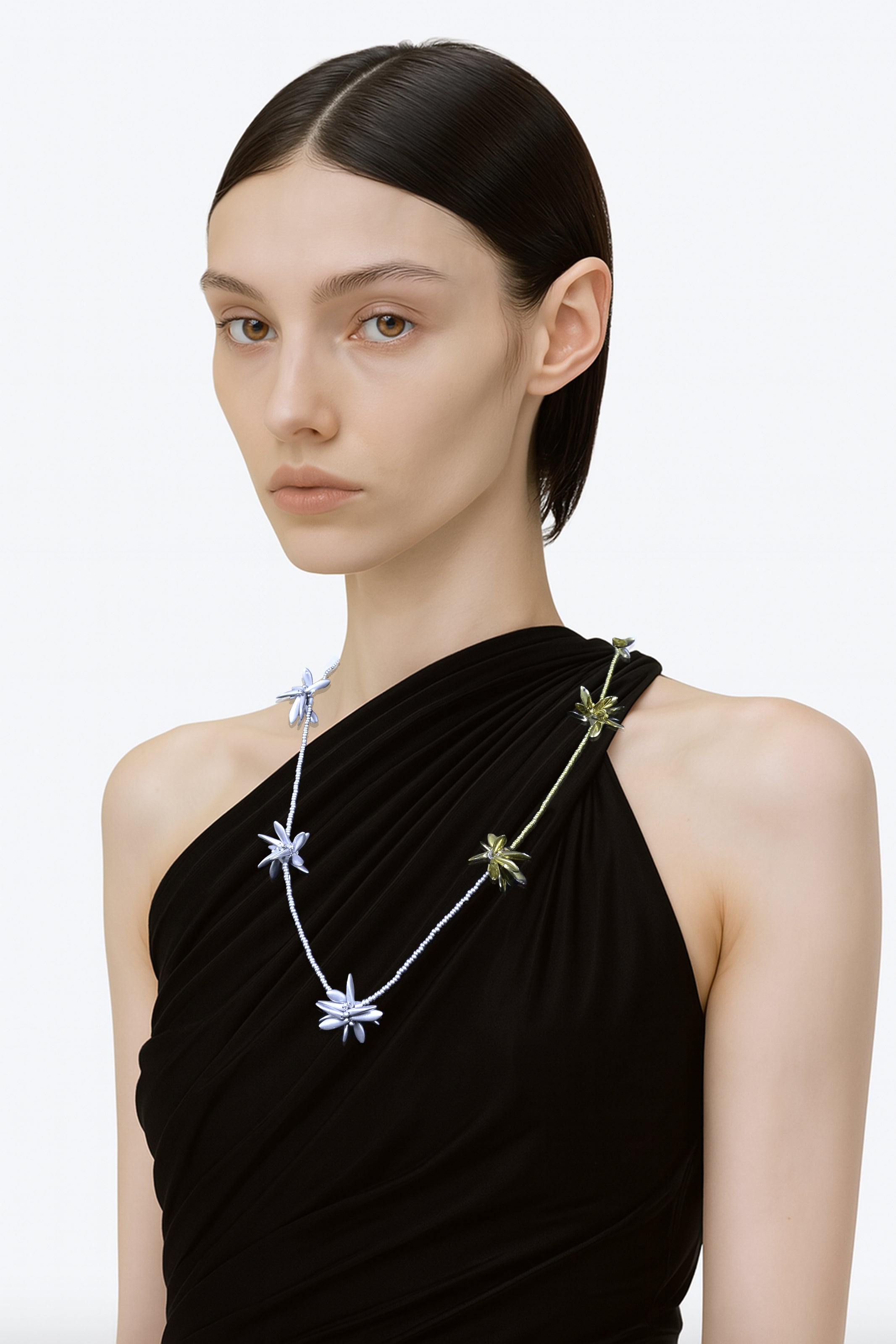 Model wearing a black one-shoulder dress with a floral-shaped bicolour beaded necklace on a white background