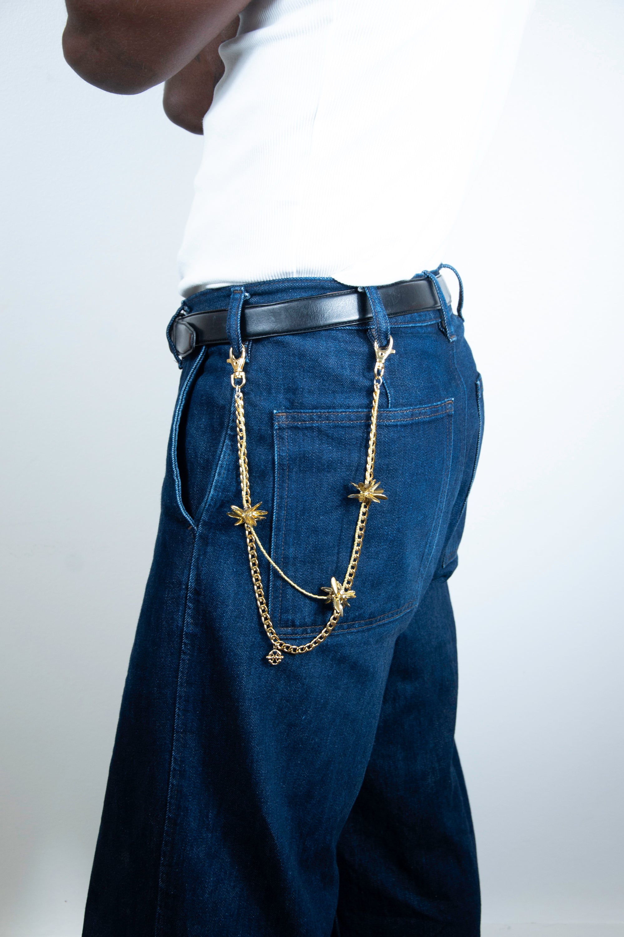 Model wearing a pants chain with gold floral-shaped beaded elements on denim trousers