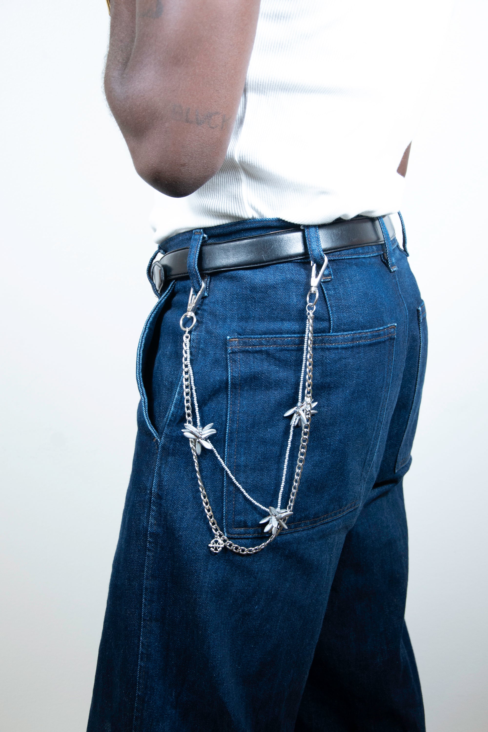 Model wearing a pants chain with silver floral-shaped beaded elements on denim trousers