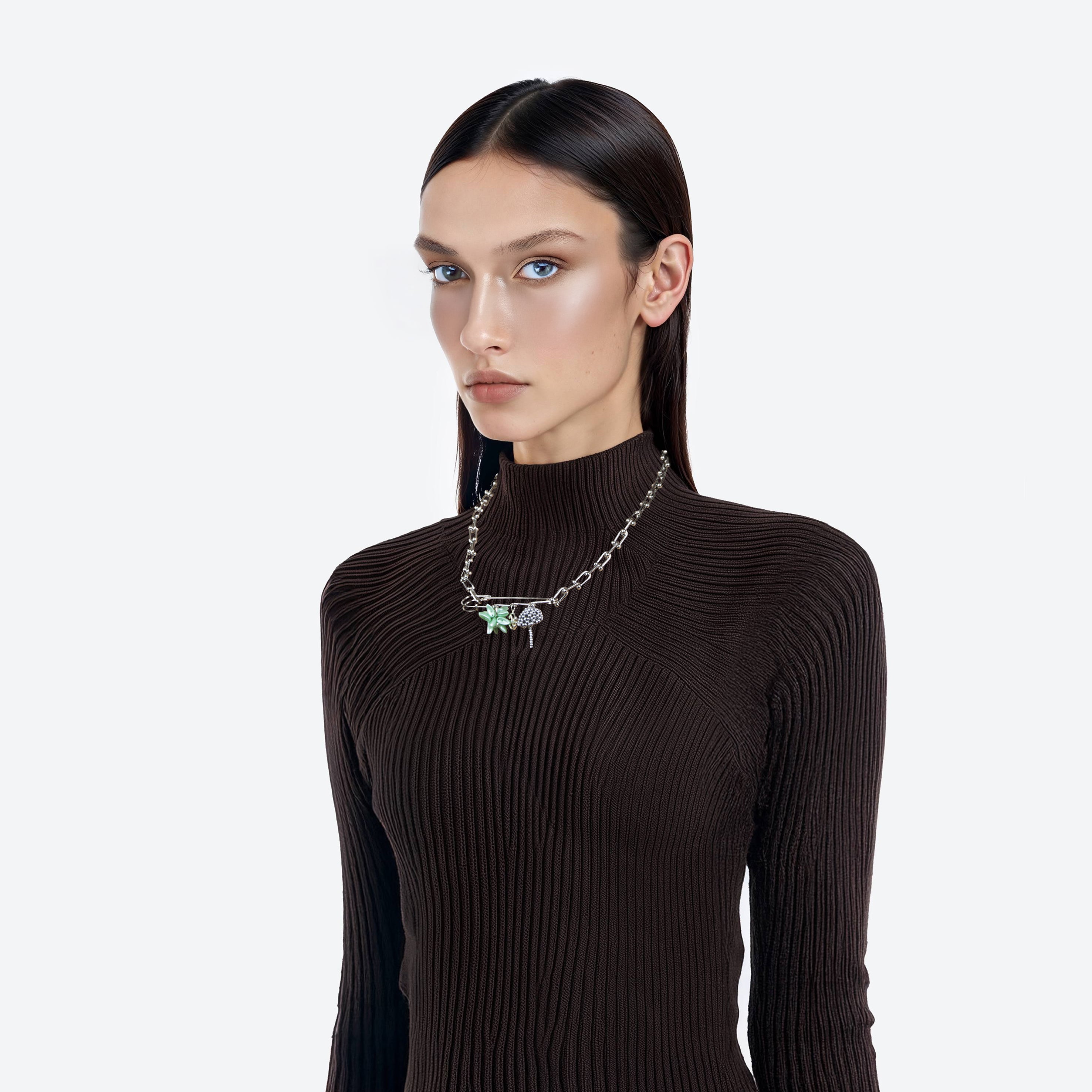 Woman wearing a dark ribbed sweater and a beaded fantasy necklace with a green pendant on a brooch and chain on a white background