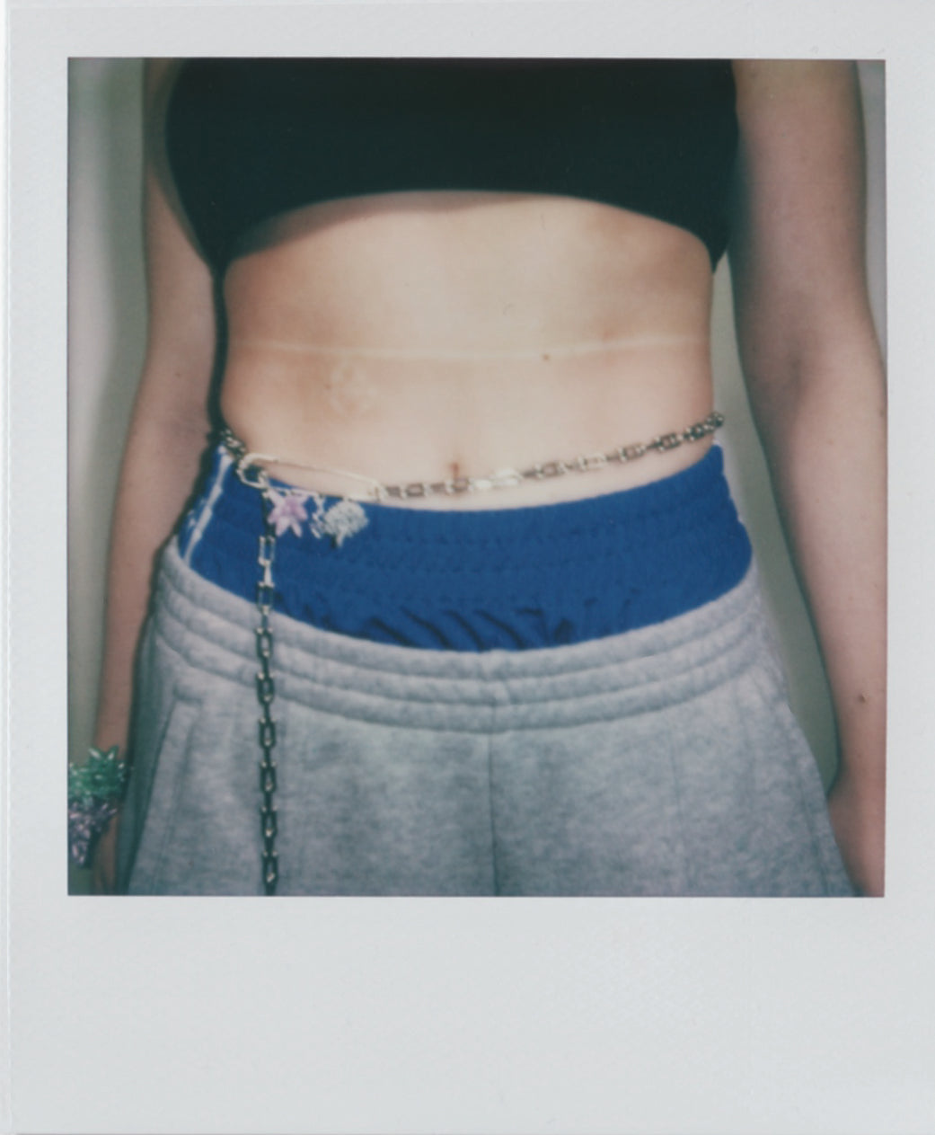 stainless steel bellychain with multi charms brooch and beaded mushroom in silver beads and an acid purple beaded flower on a model on a polaroid picture
