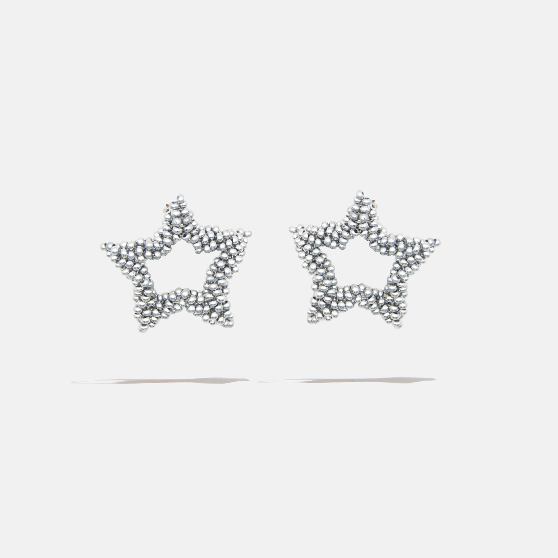 Silver star-shaped earrings with bead detailing on a light gray background