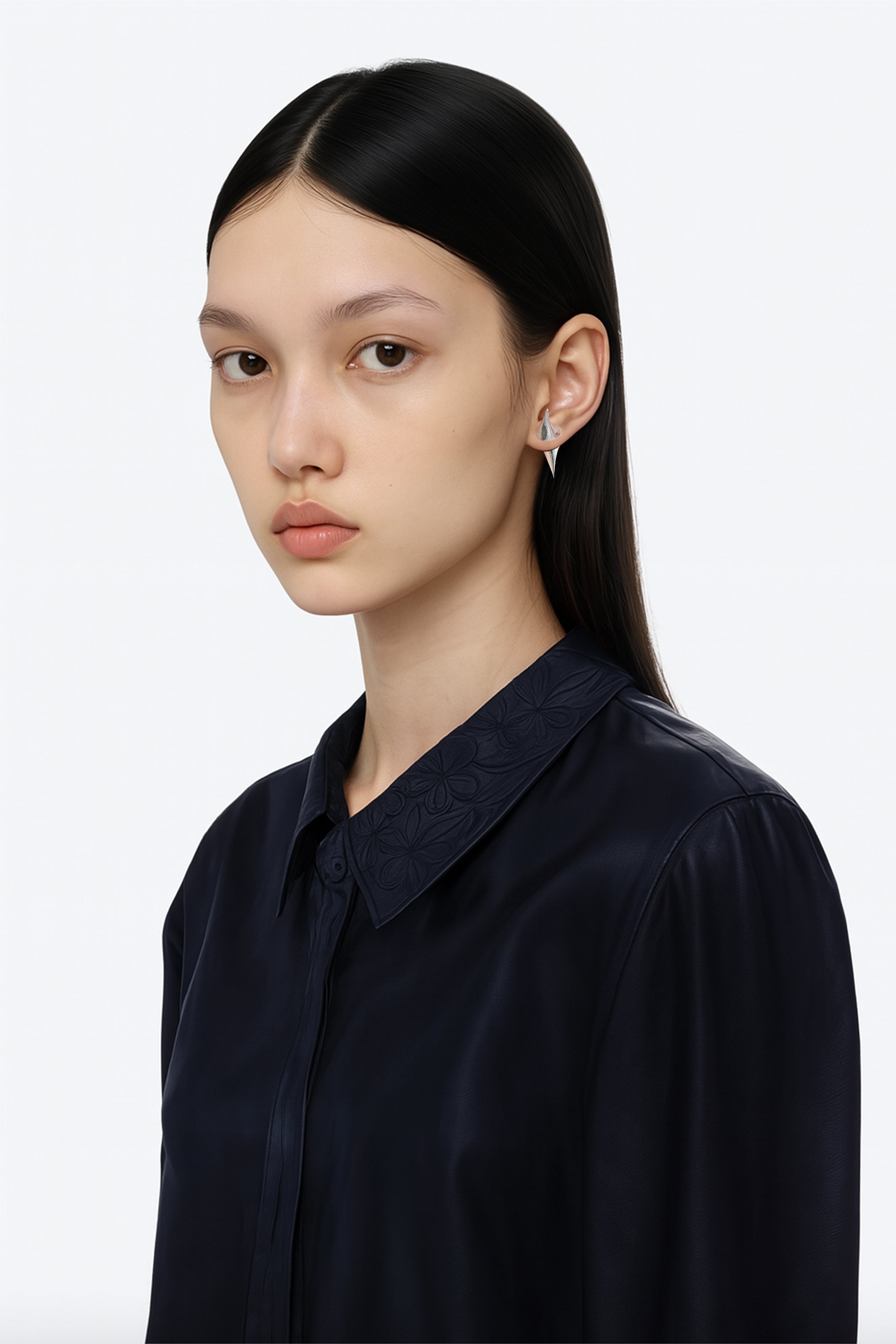 A brass silver pair of spikes stud earrings worn by an AI model with leather black tailored jacket and long dark hair view from 3/4