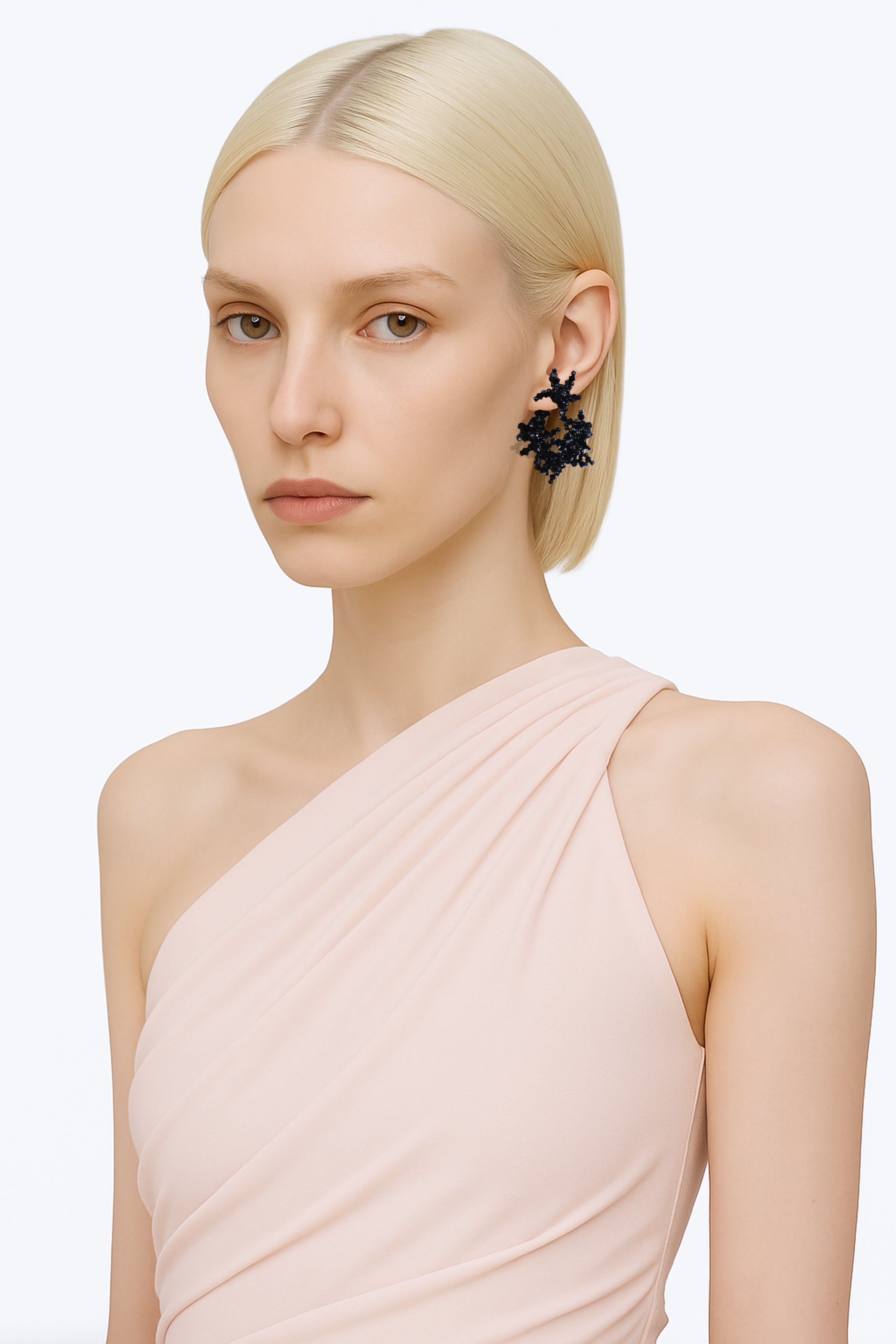 A brass black handcrafted beads hoop stud fantasy earring worn by an AI model with powder pink top and short polar blonde hair view from 3/4
